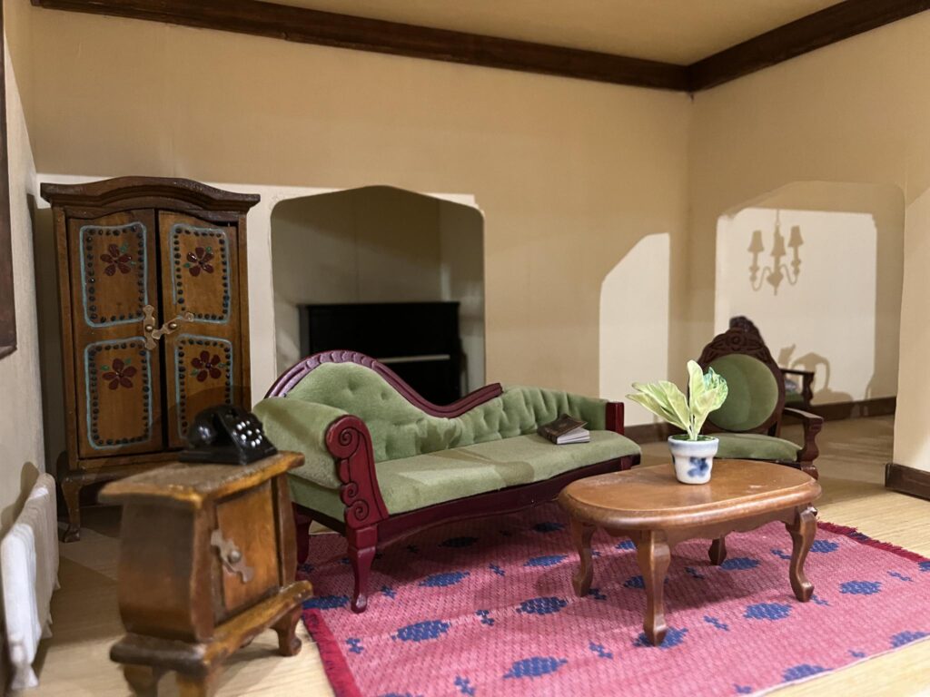 A miniature recreation of a living room, with a chaise lounge, armoire, coffee table, piano, and rug.