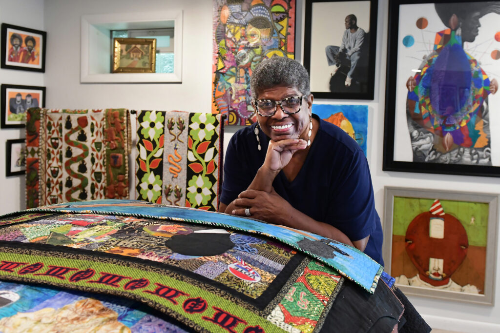 Dark-skinned woman smiles on a pile of quilts.