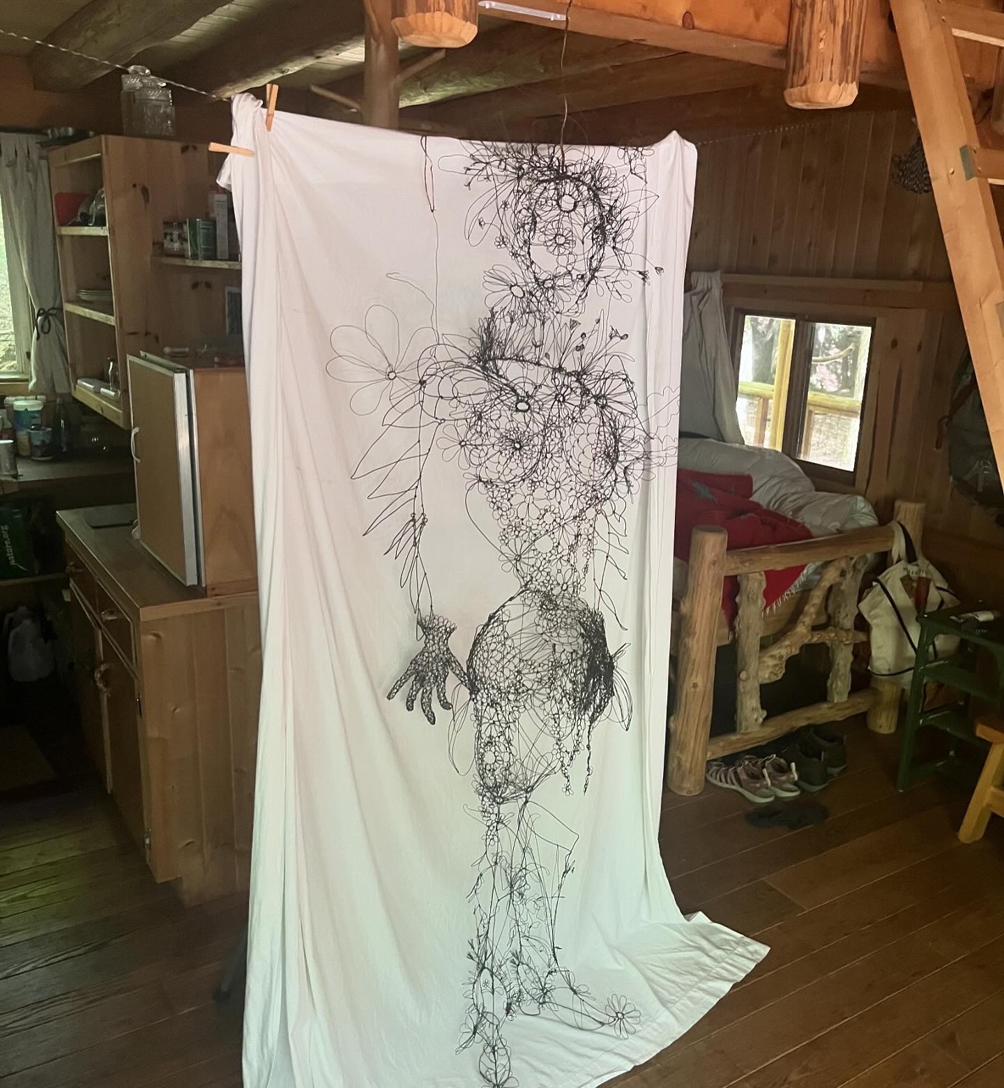 A wire sculpture hanging in front of a sheet inside a cabin.