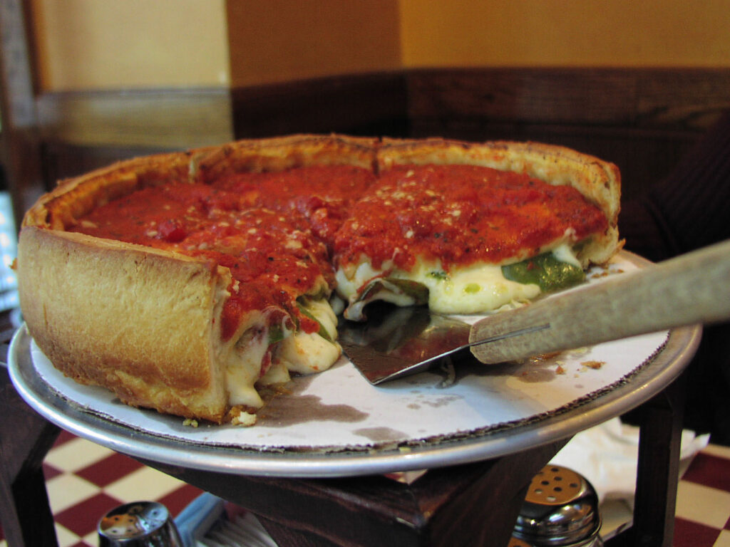 A circular, deep-dish pizza with tall sides. It has been cut into and has red tomato sauce on top and gooey cheese on the inside.