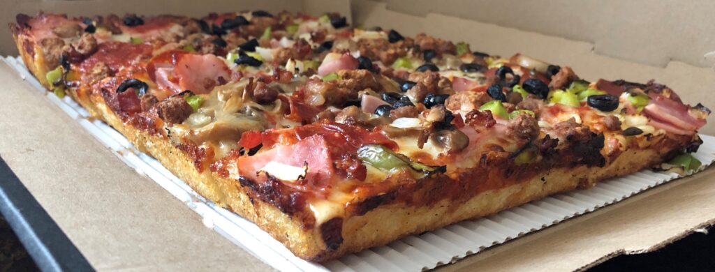 A rectangular pizza with multiple toppings in an open cardboard box.