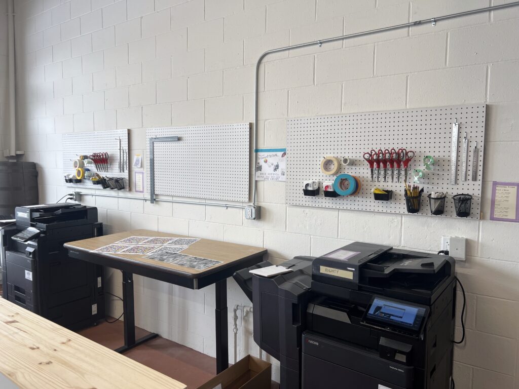 An indoor workshop with tables, copy machines and a pegboard holding tools.