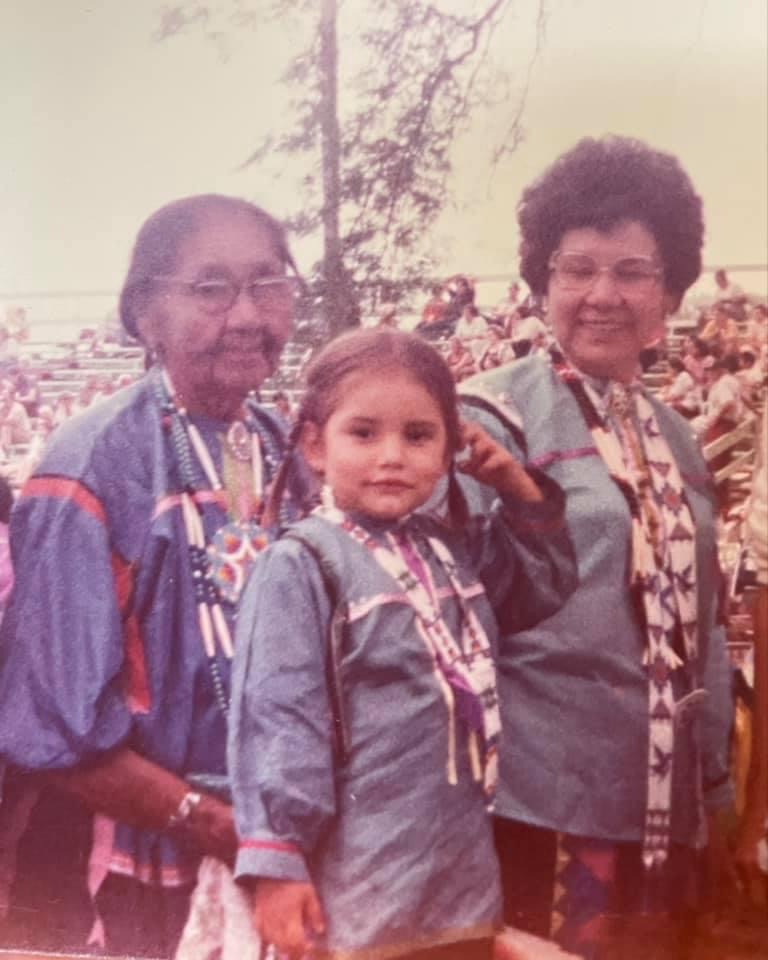 Archival photo of two adults and a young person. They are wearing traditional regalia.