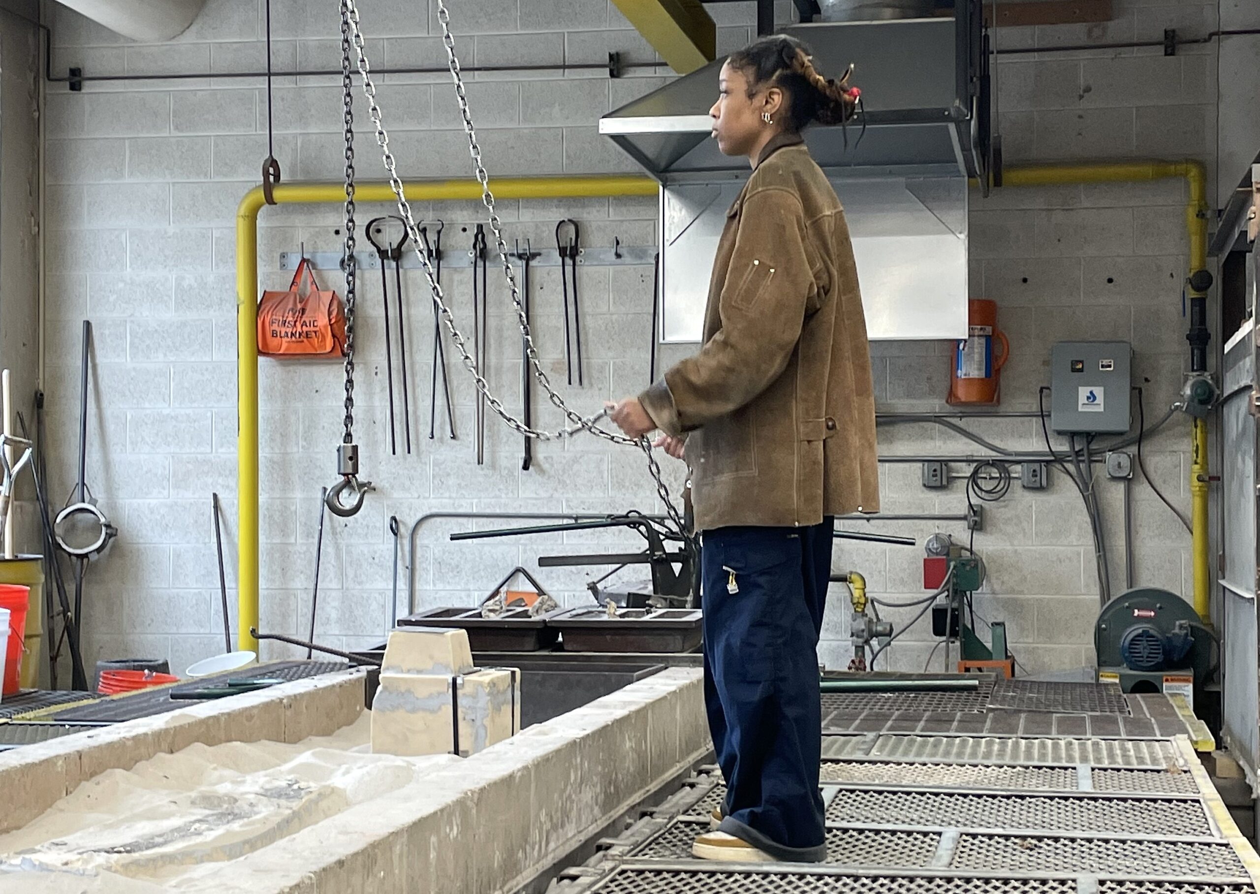 A person stands to the side and holds two pieces of metal chains in a workshop room.