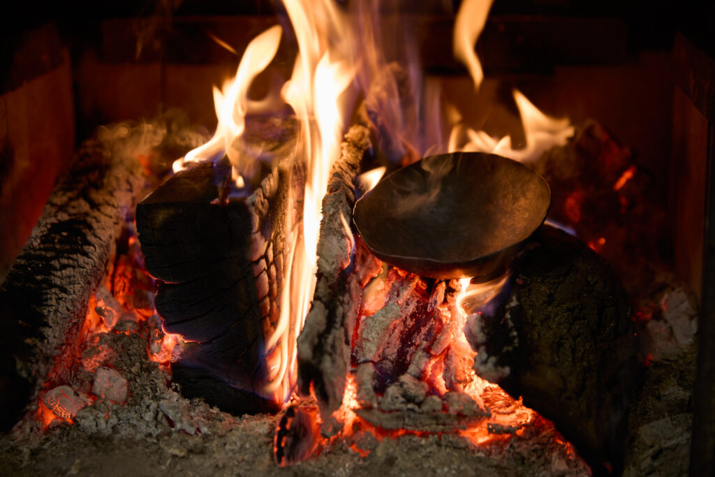 A copper bowl being held over a fire.