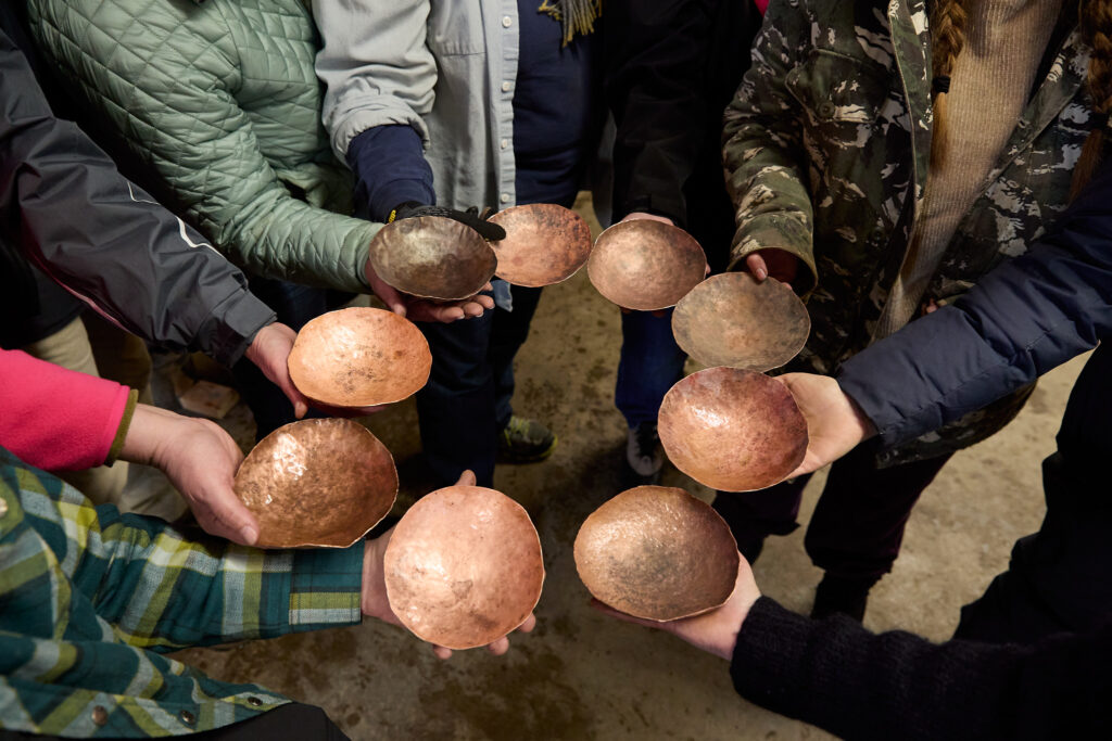 A circle of people holding out their copper bowls.