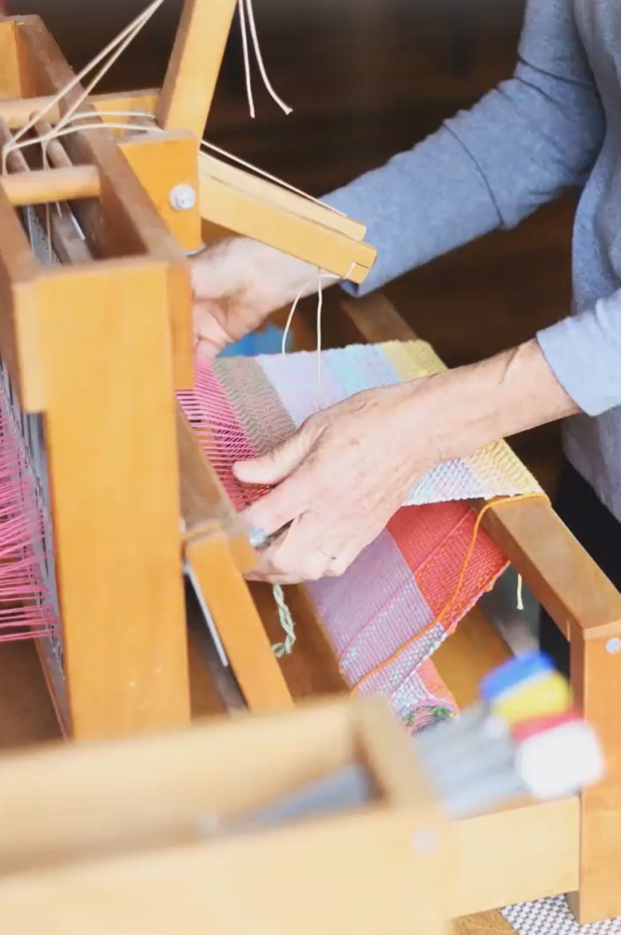 Older hands from a light-skinned person work a wooden loom.