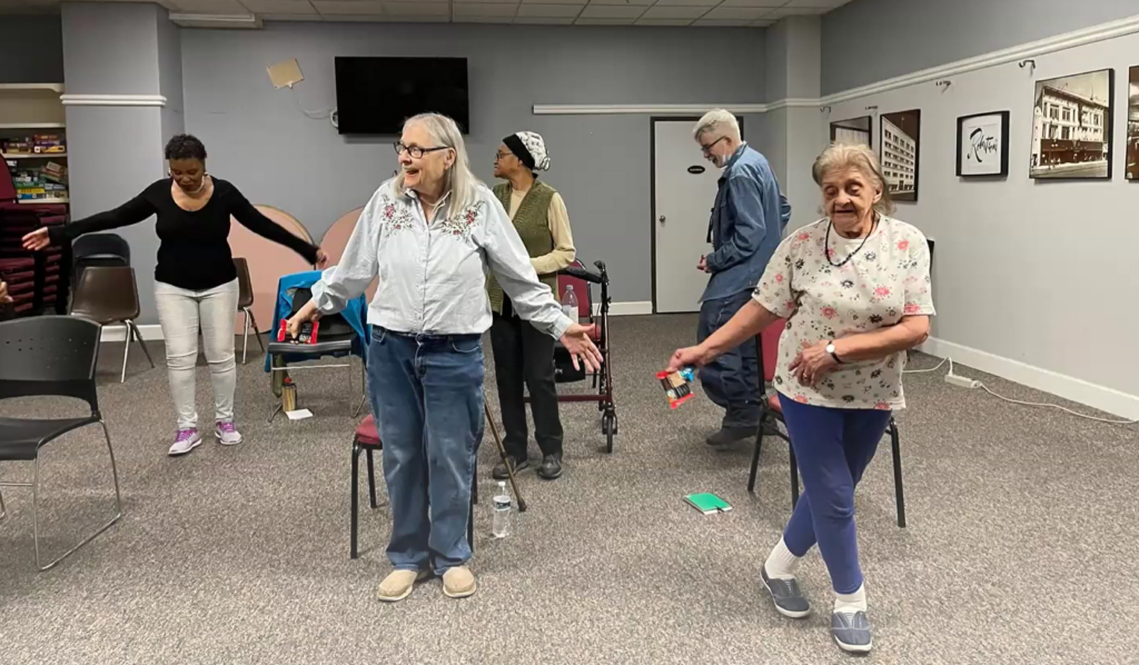 A handful of older adults stand and swing their arms.