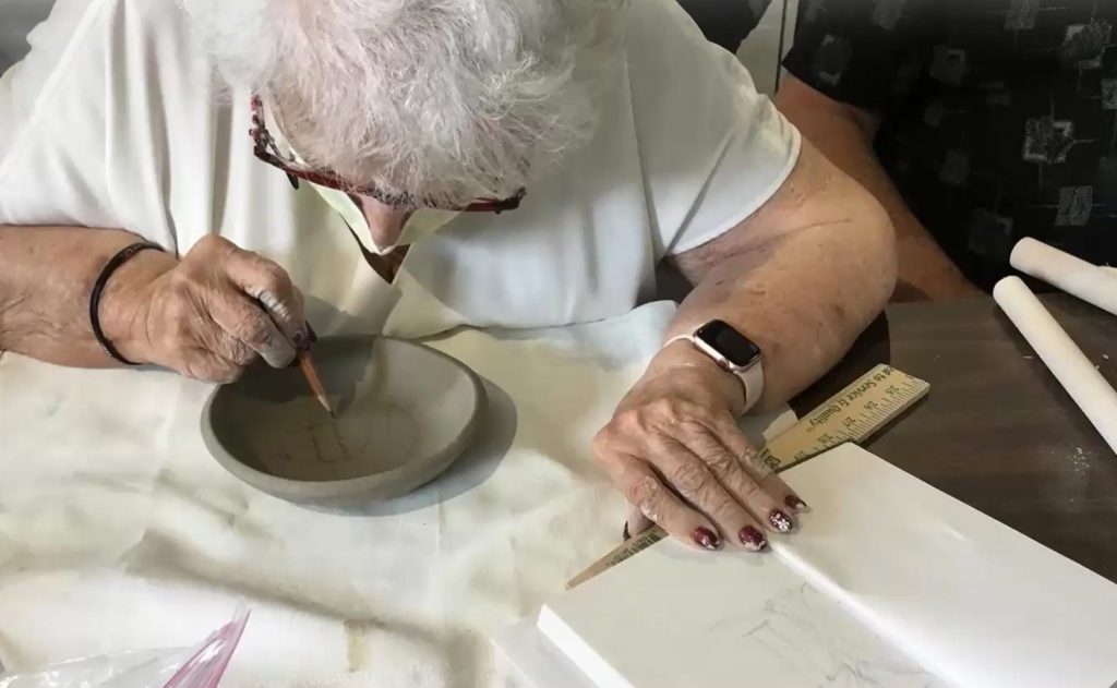 A light-skinned woman looks down at a piece of art she is creating on a table.