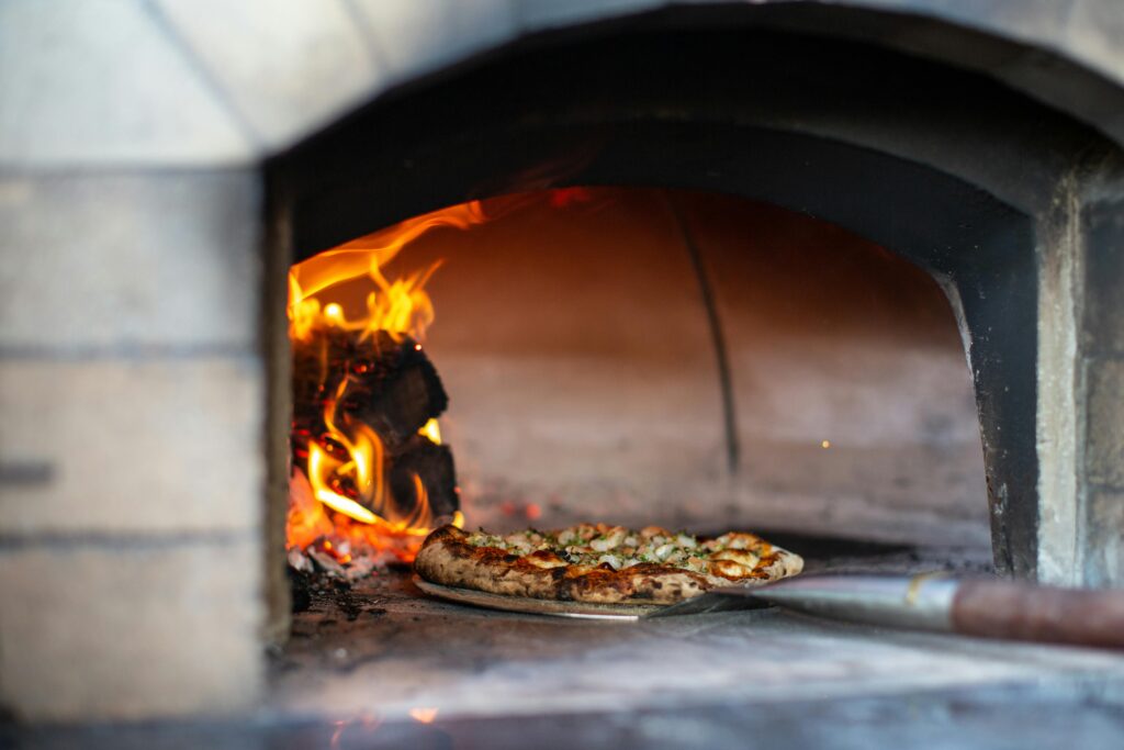 A pizza getting pulled out of a wood fire oven.