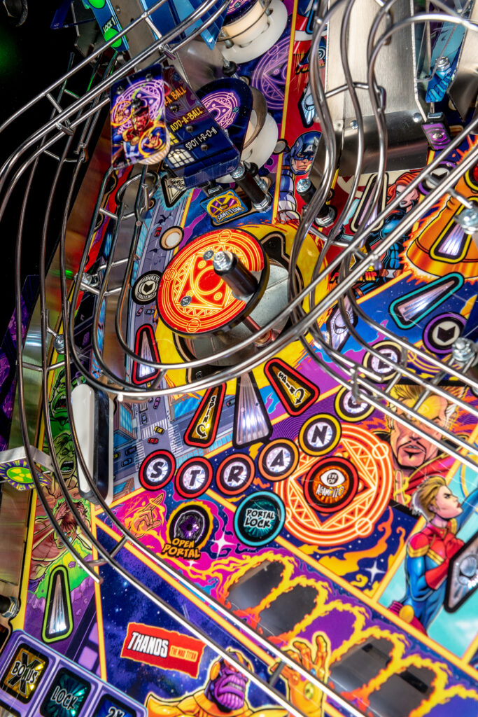 Close-up of a brightly colored Avengers-themed pinball playfield featuring Doctor Strange’s mystical symbols, character portraits like Captain Marvel and Hulk, and neon game elements like "Open Portal" and "Portal Lock."