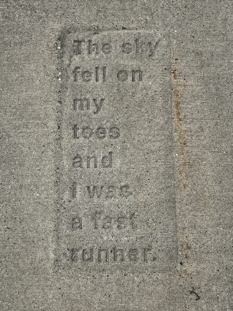 A poem stamped in dry concrete reads: "The sky fell on my toes and I was a fast runner."