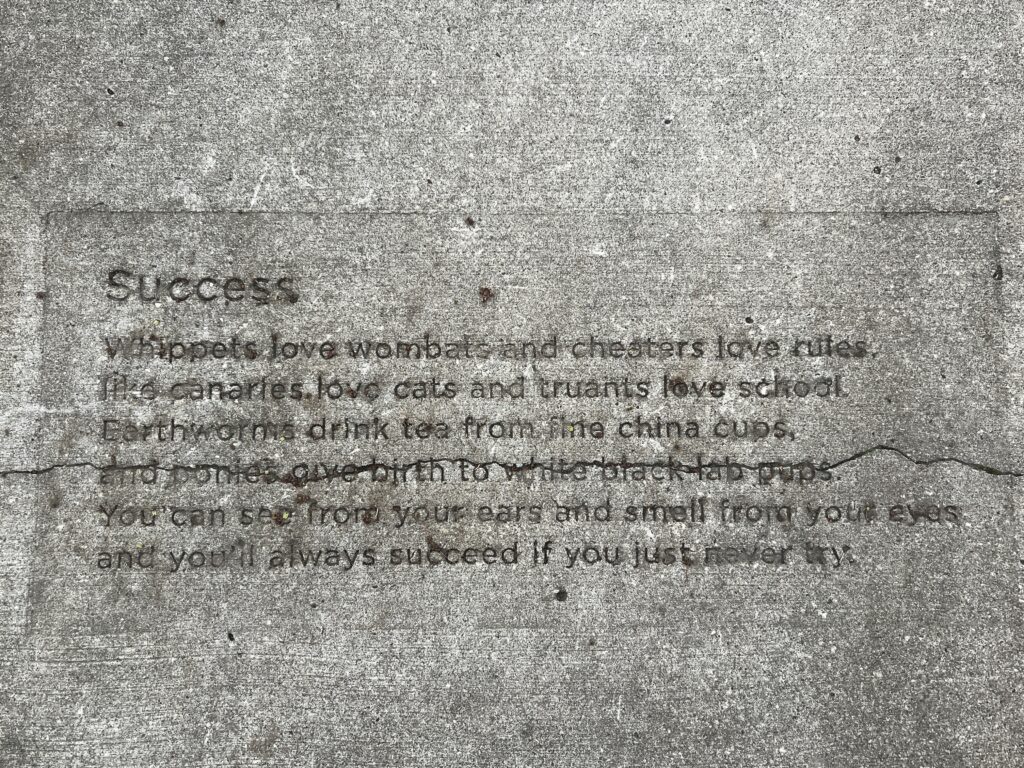 A poem titled "Success" is stamped on a sidewalk with a crack running through one of the lines.