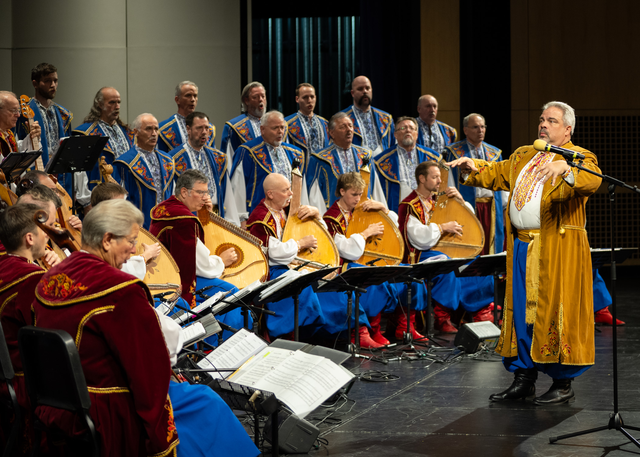 People play music and sing on a stage and a conductor stands to the right.