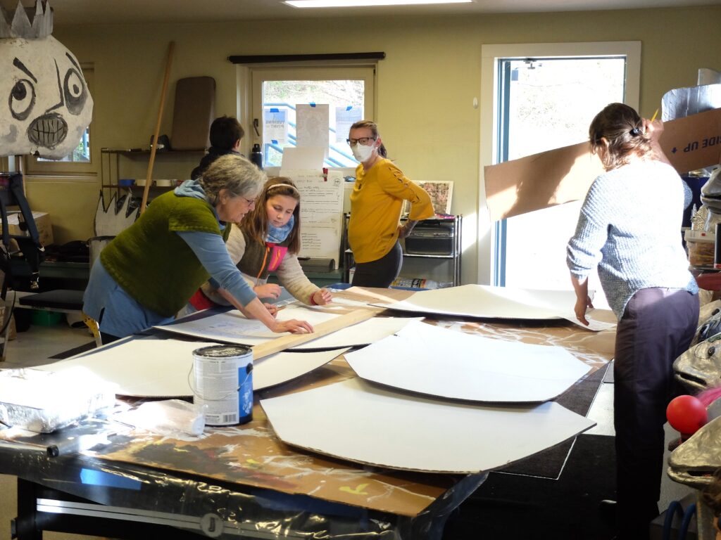 Several light-skinned people stand around a large table and adjust large pieces of cardboard.