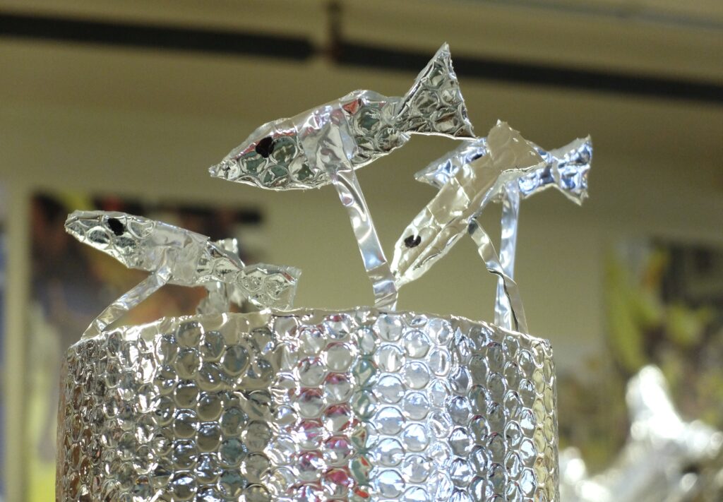 Three silver tinfoil fish are propped up on a silver piece of packaging material.