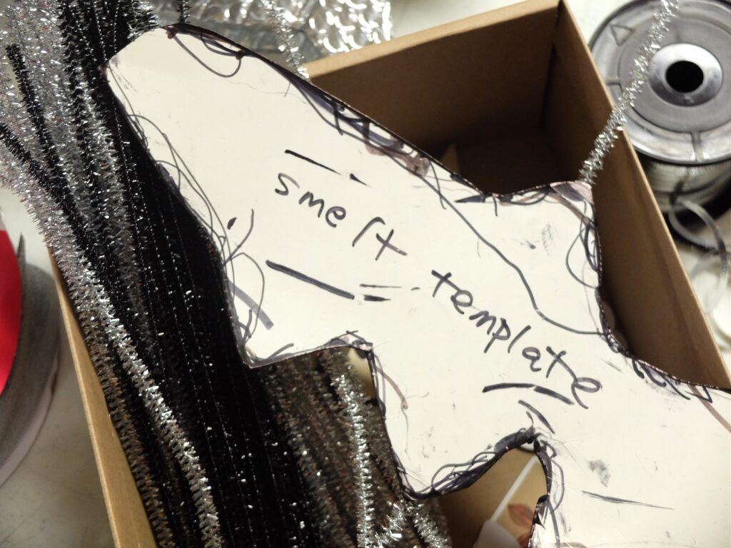 A piece of thick white paper is cut into the shape of a fish and reads: smelt template.