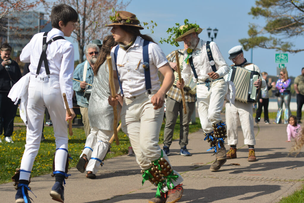 People wearing all white and black suspenders dance on a sidewalk.