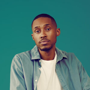 Portrait of a person with brown skin tone and short hair, wearing a teal button up and white shirt, on a teal background.