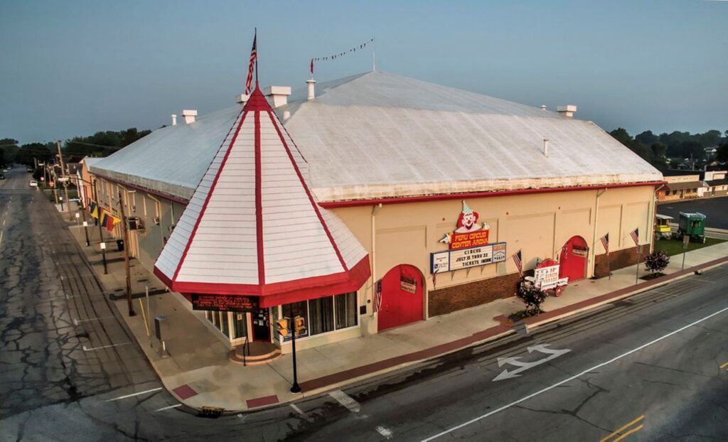 A large building painted white, red, and beige. The entrance is a corner door with a large cone-shaped covering on top of it.
