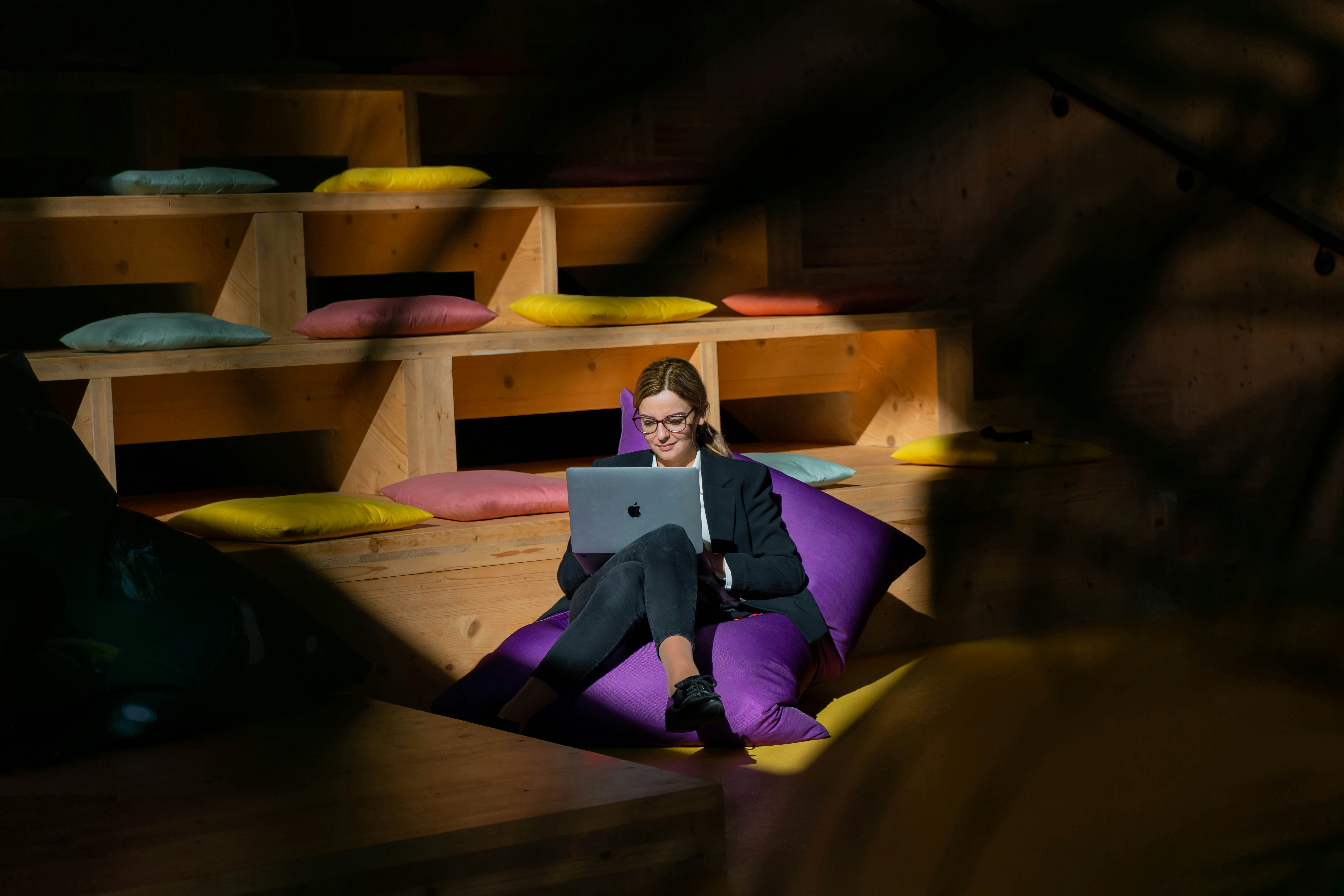 A smiling person sitting on a beanbag typing on a laptop.