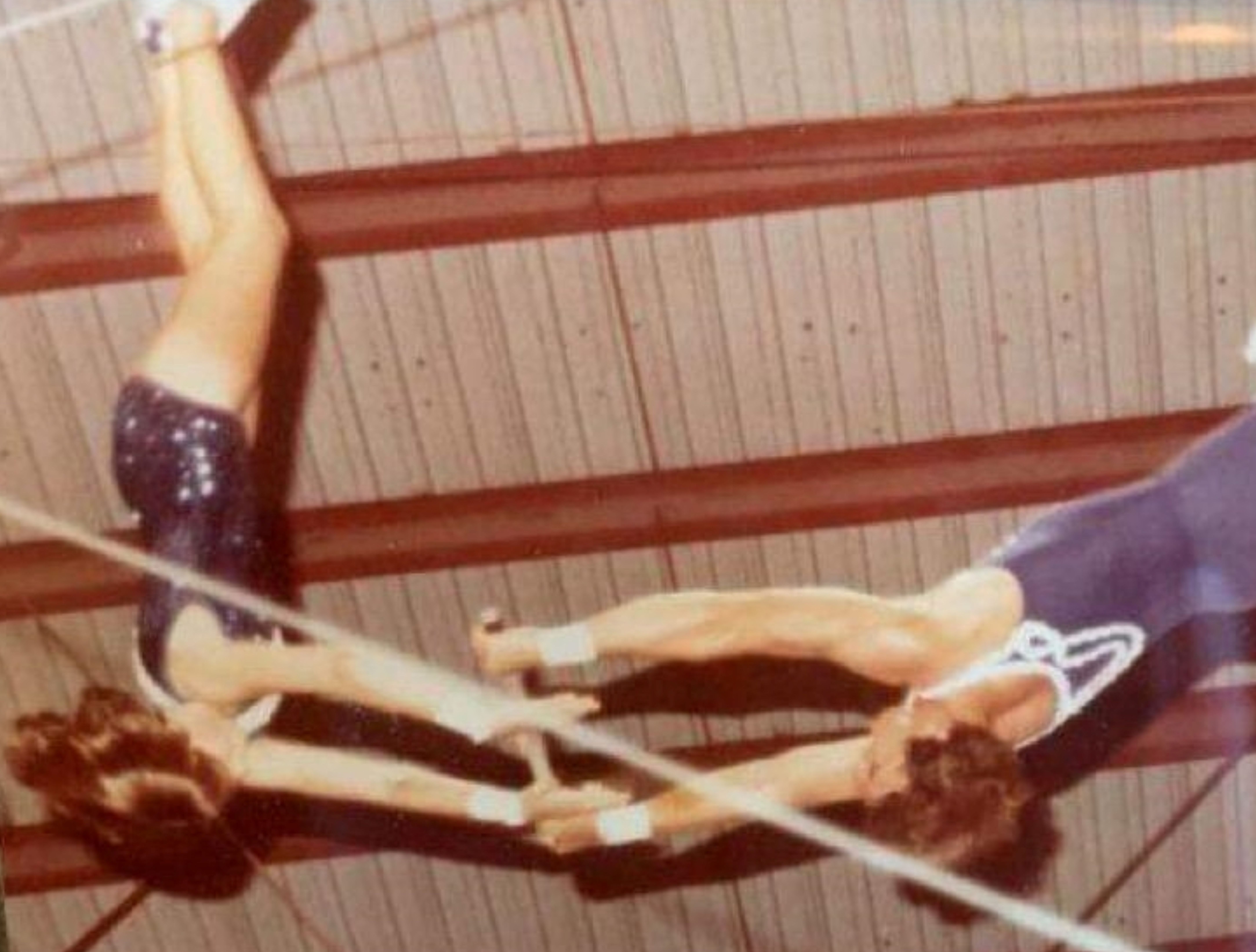 An archival photo of two people mid-air upside down with both of them reaching for a trapeze bar.