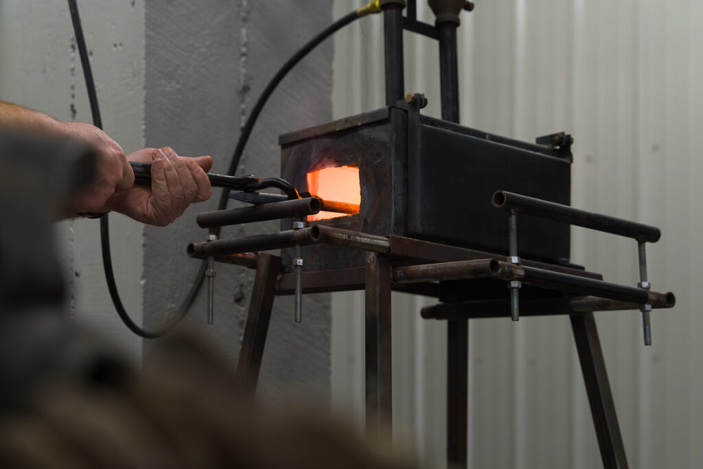 Light-skinned hands hold metal into a hot forge.