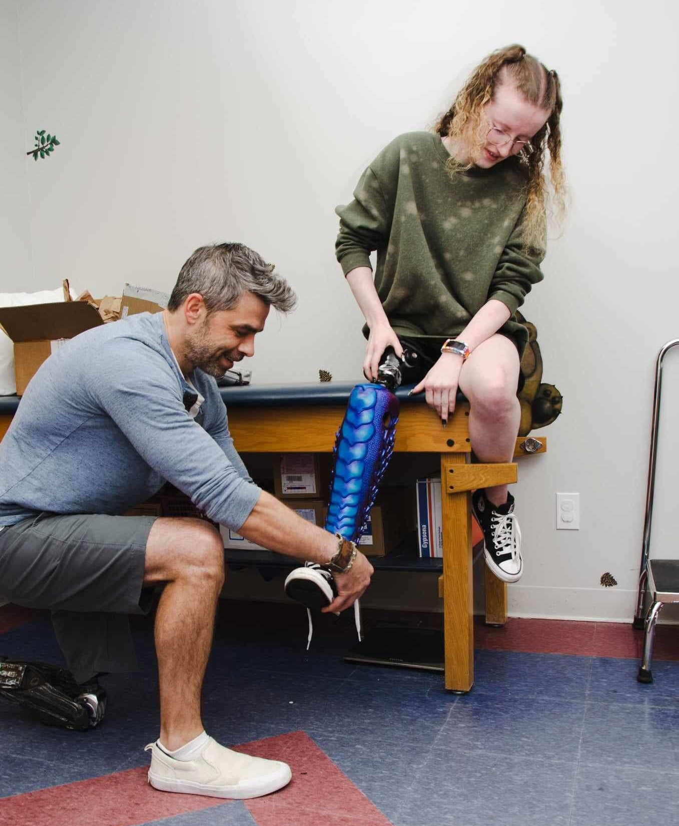 A person kneeling and helping another person put on a prosthetic leg.