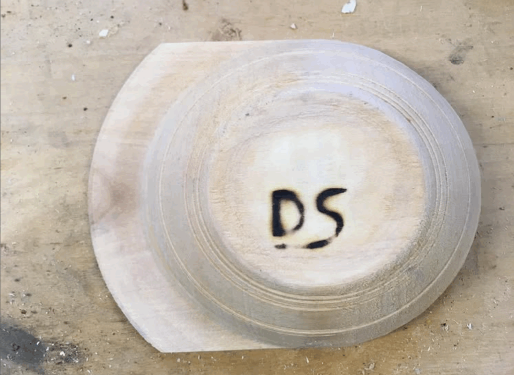 An upside down wooden bowl with the letters D and S burned into it.