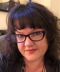A white woman with brown hair and glasses smiles at the camera.