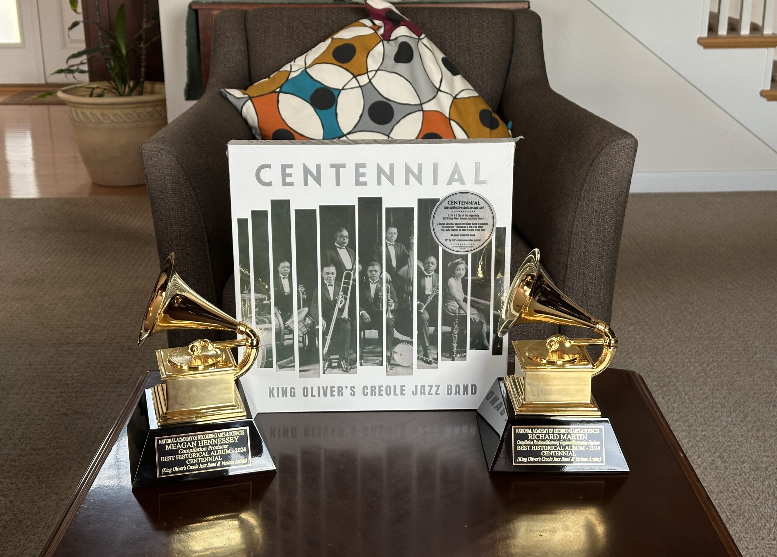 A music vinyl record sleeve rests on a table next to two Grammy award trophies.