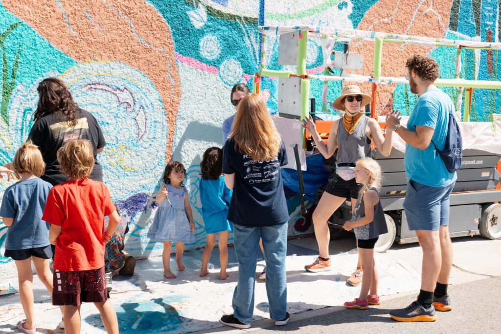 People gathered around a mural in progress.