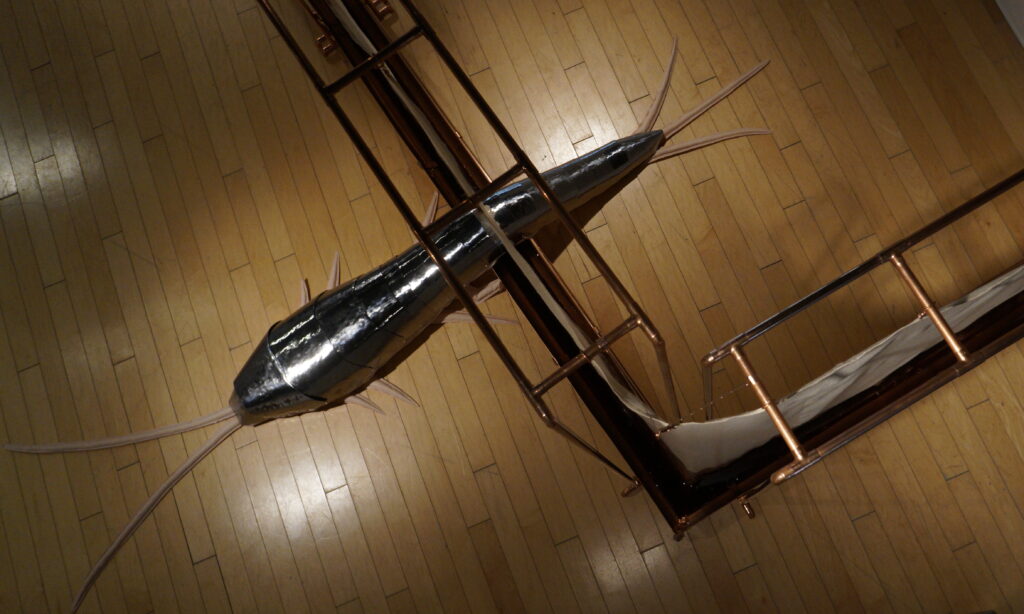 A large silver insect with long antennae at its head and tail crawling through a barrier of metal and latex.