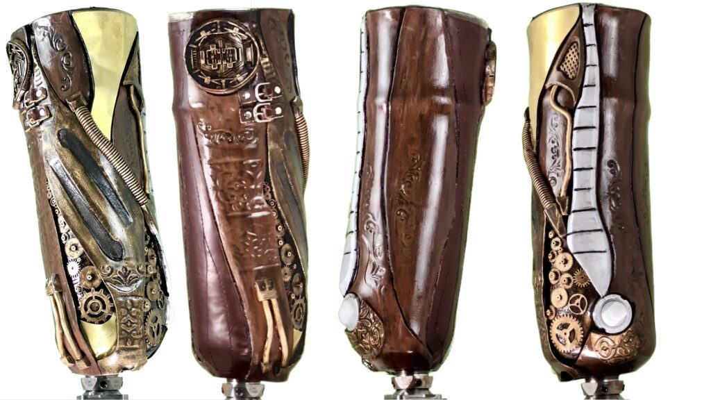 A custom prosthetic socket designed in a steampunk style. The surface is detailed with embossed floral patterns, metallic gears, pipes, coils, and rivets in bronze, brass, and copper tones. The socket has an industrial, sculptural look with layered textures and mechanical ornamentation.