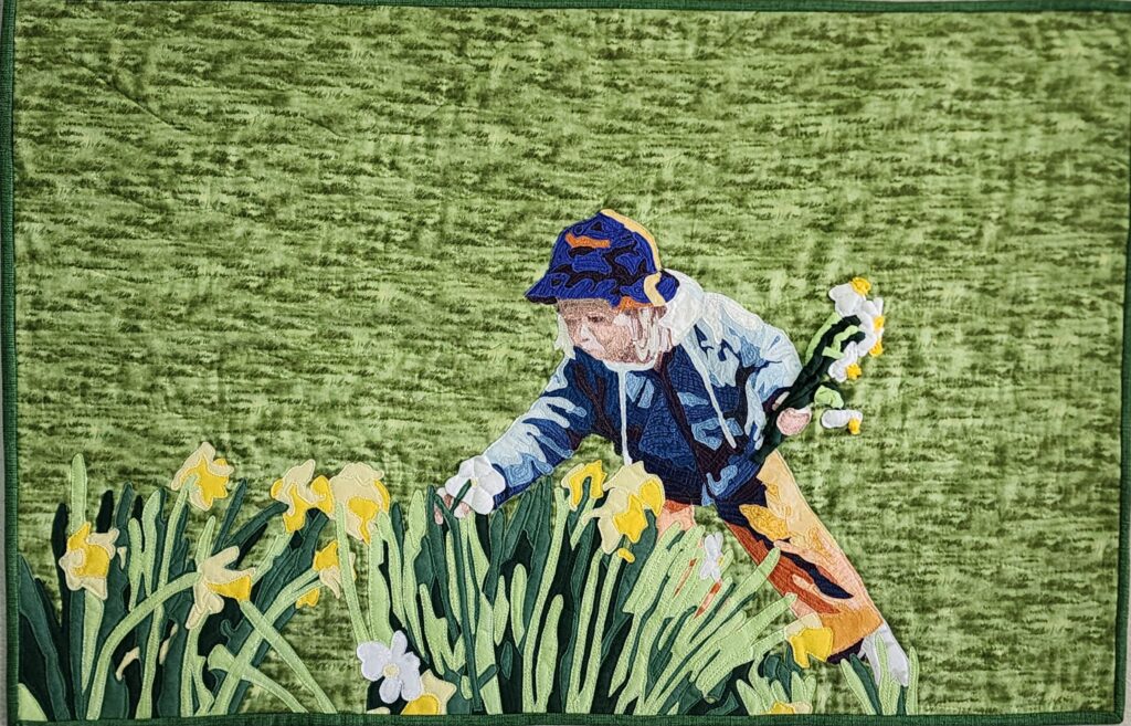 A figure with light skin tone and white-blonde hair, a blue bucket hat and sweatshirt, and orange pants holding five daffodils in one hand and leaning down to pick another from a patch of yellow and white daffodils against a grassy green background.
