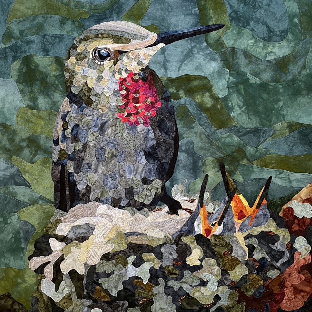 A gray-green hummingbird with a bright red patch on its neck is perched on a nest with two hatchlings inside, with their orange beaks wide open toward the sky.