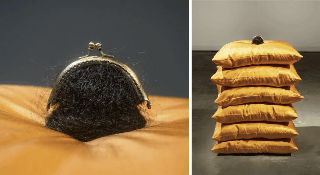 A bundle of dark hair topped with a brass purse clasp resting on a neat stack of six golden-orange silk cushions.