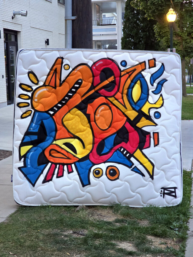 A white mattress outside painted with a colorful abstract piece.