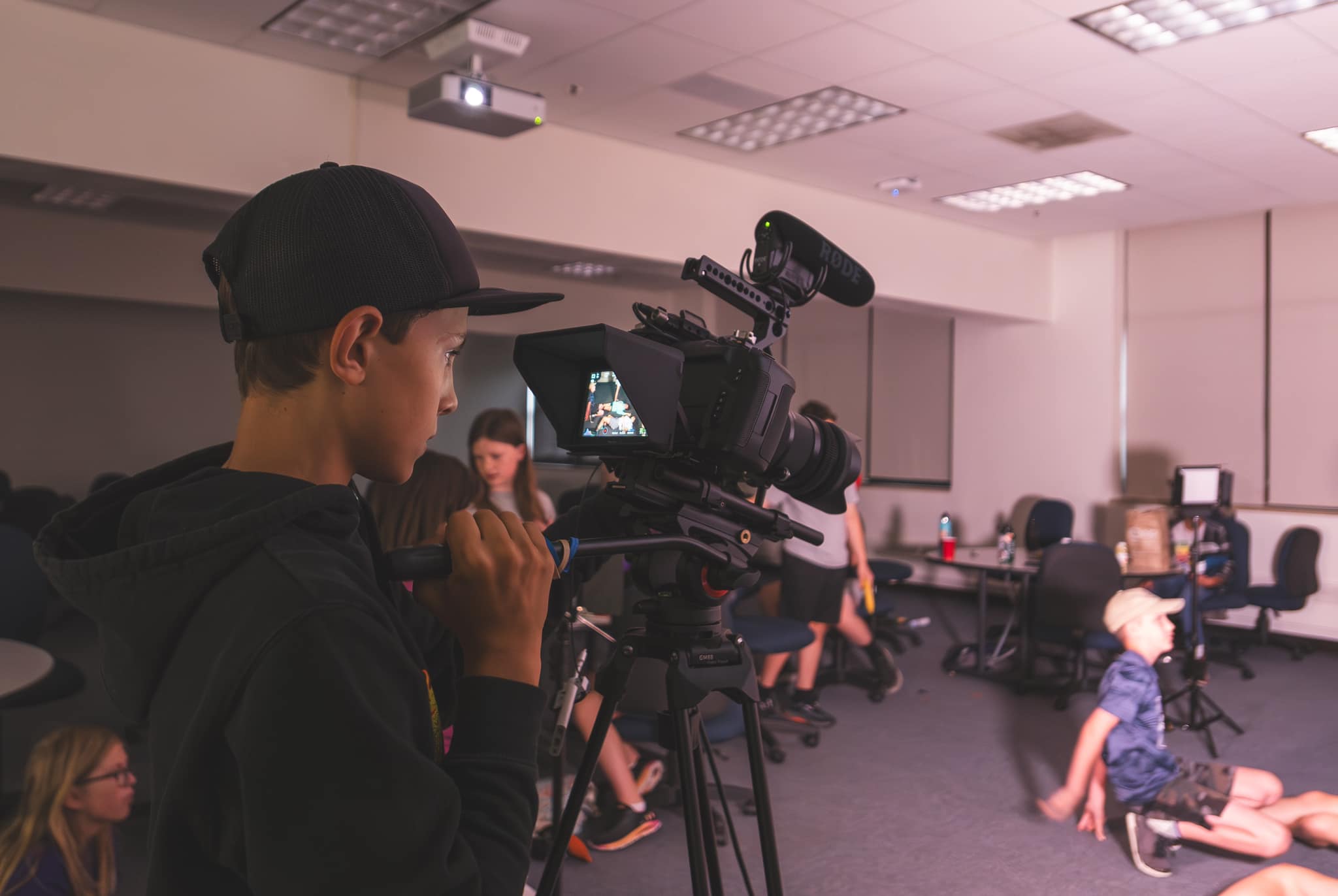 A young person looks into a screen of a video camera as they are filming a scene in front of them.