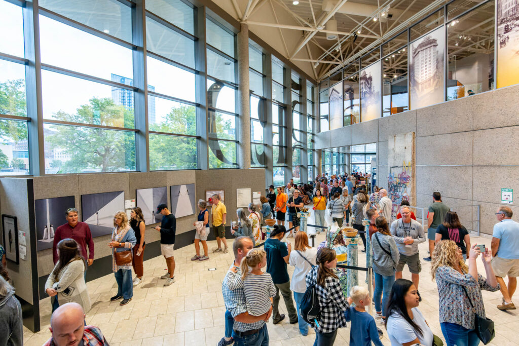 A large room with tall ceilings filled with people looking at art on the walls.