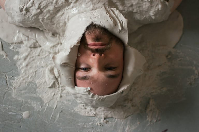 a person with light skin upside down and inside of a clay cast.