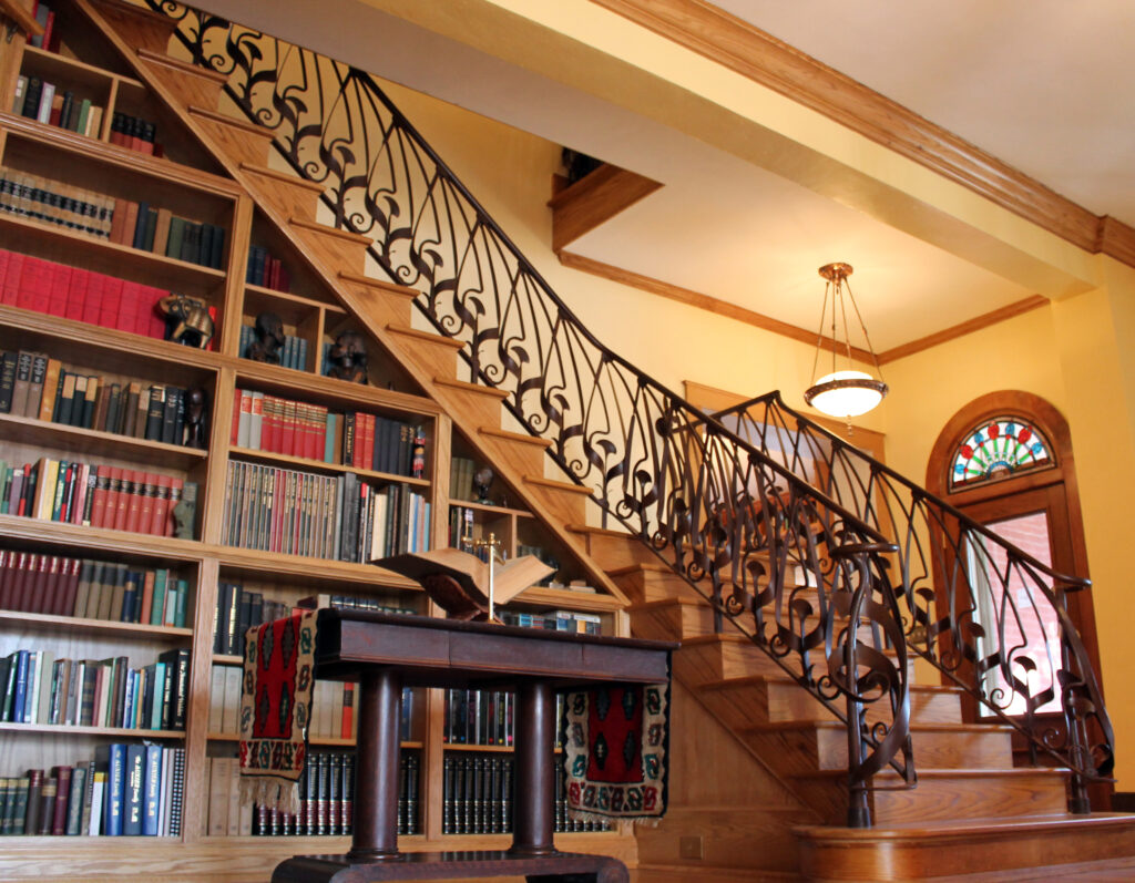 A wooden staircase with ornate black wrought iron railings beside built-in bookshelves filled with books and sculptures.
