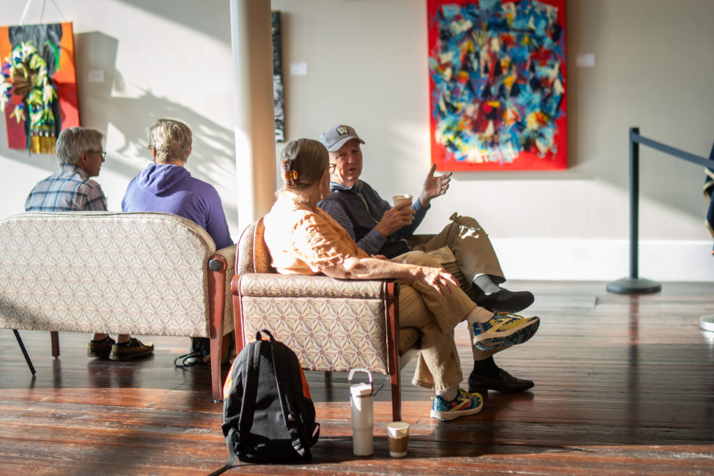 Group of people sitting on couches in an art gallery, talking and enjoying the displayed artwork.