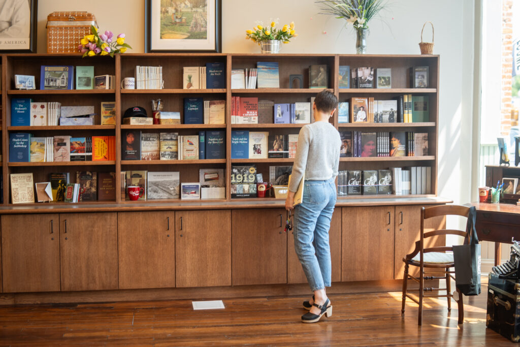Person standing in front of a wooden bookshelf lined with Willa Cather books and memorabilia inside a bright shop.