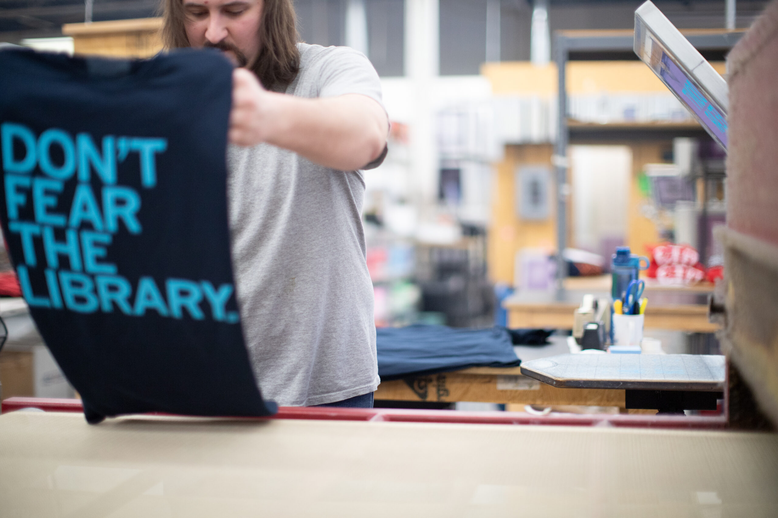 Person holding up a shirt reading: Don't Fear The Library.