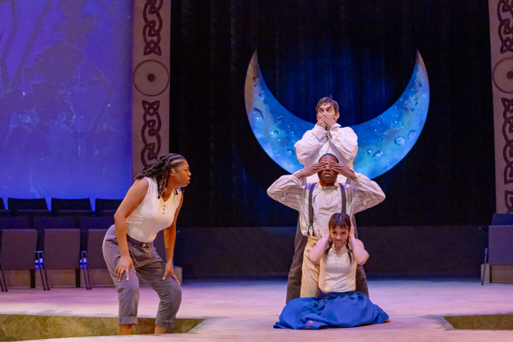 Four actors perform a scene from A Midsummer Night's Dream at Cincinnati Shakespeare Company, with a large crescent moon hanging as a back drop.