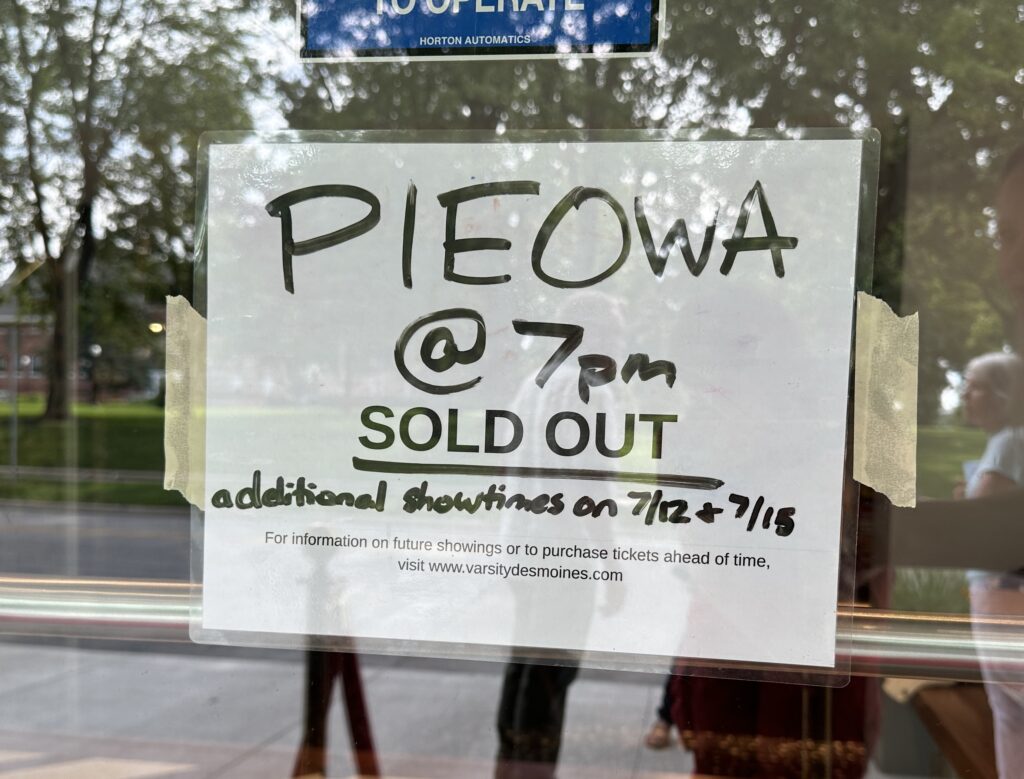 A handwritten sign taped to a glass door reads, “PIEOWA @ 7pm SOLD OUT. Additional showtimes on 7/12 + 7/15.”
