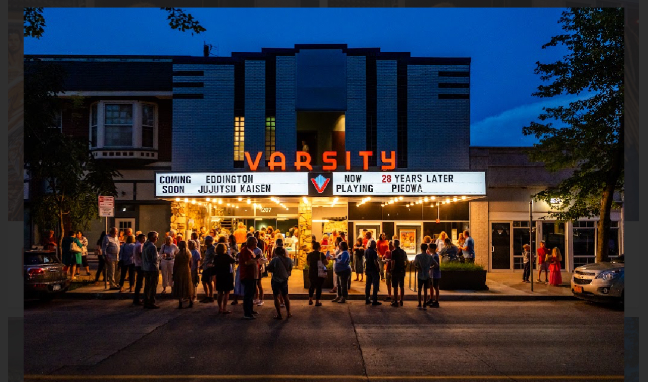 People stand clustered outside a warmly lit movie theater. The marquee reads Now Playing: Pieowa