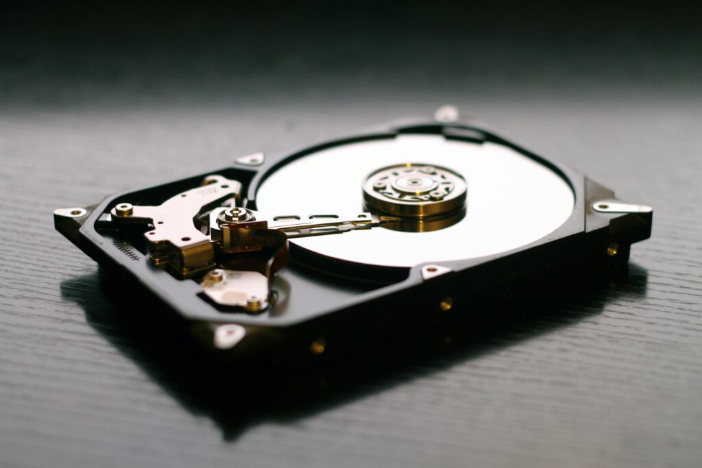 A close-up of an open hard disk drive showing the circular platter and read/write arm, resting on a dark wooden surface.