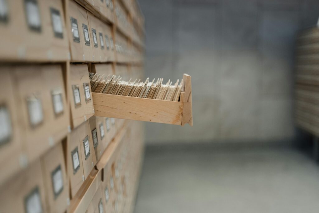 A wooden filing cabinet with one drawer open, filled with rows of organized paper files.